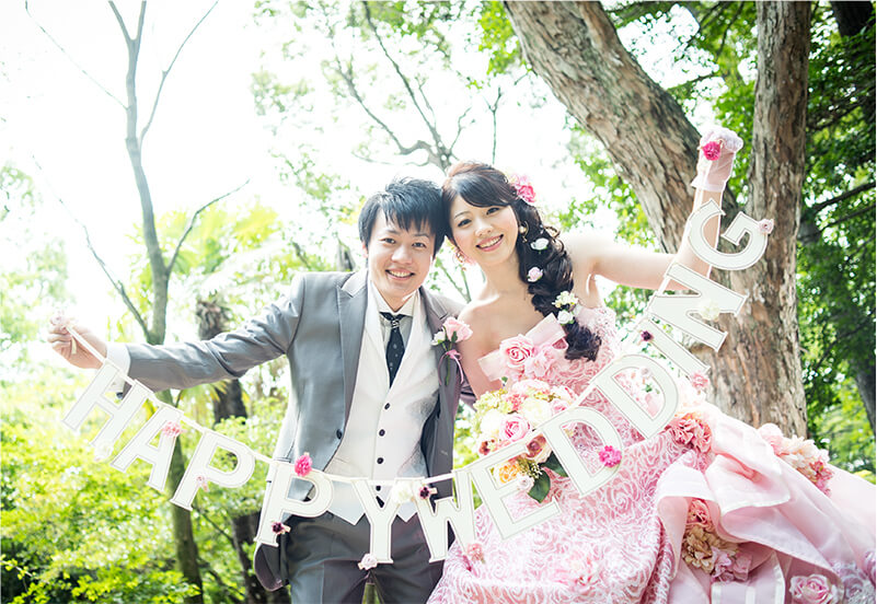 洋装姿のカップルが「HAPPY WEDDING」と書かれたアイテムを持っているイメージ
