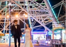Nagoya Port Sea Train Land｜洋装姿のカップルが夜の遊園地で観覧車を背景に撮影をしているイメージ