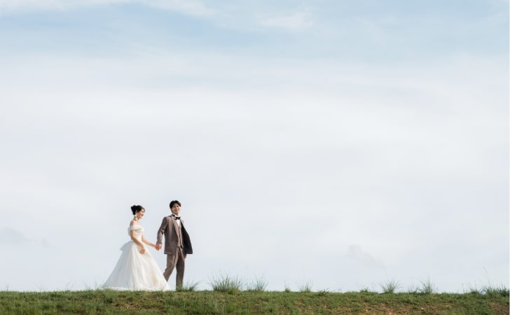 Shounai Ryokuchi Park｜洋装姿のカップルが草原の上で空を背景に撮影しているイメージ