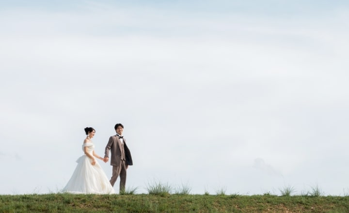 Shounai Ryokuchi Park｜洋装姿のカップルが草原の上で空を背景に撮影しているイメージ